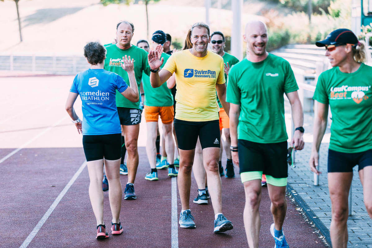 Ein Foto aus der Lauftrainer Ausbildung der Laufcampus Akademie. Nach dem Training klatschen sich etwa zehn erwachsene Läuferinnen und Läufer mit glücklichen Gesichtern ab. Eine Szene aus einer Ausbildung zum Firmenlauftrainer.